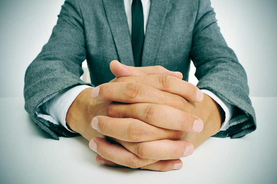 man wearing a suit sitting in a table with clasped hands